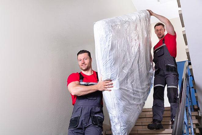 two people carrying a box spring out of a bedroom in Tallmadge